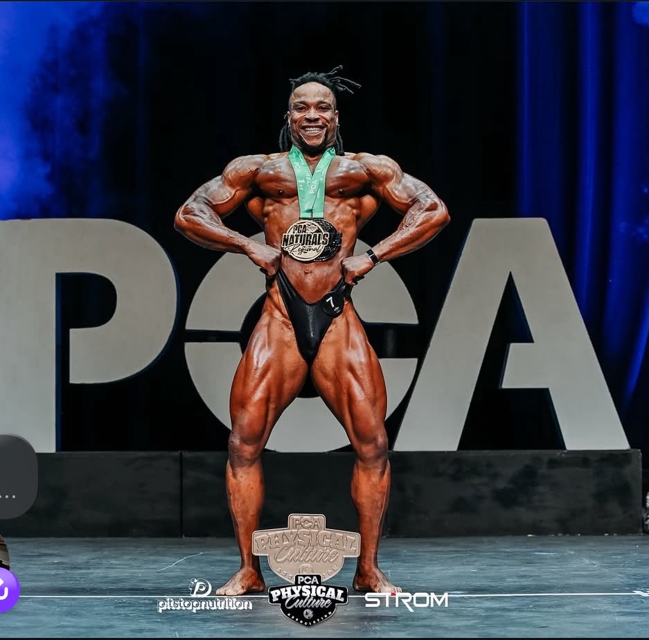 Christian Ebor posing on stage with a medal at a PCA Physical Culture bodybuilding event